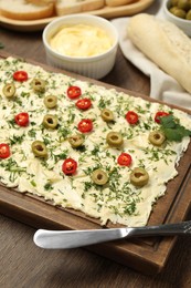 Photo of Fresh natural butter board with cut olives, pepper and knife on wooden table, closeup