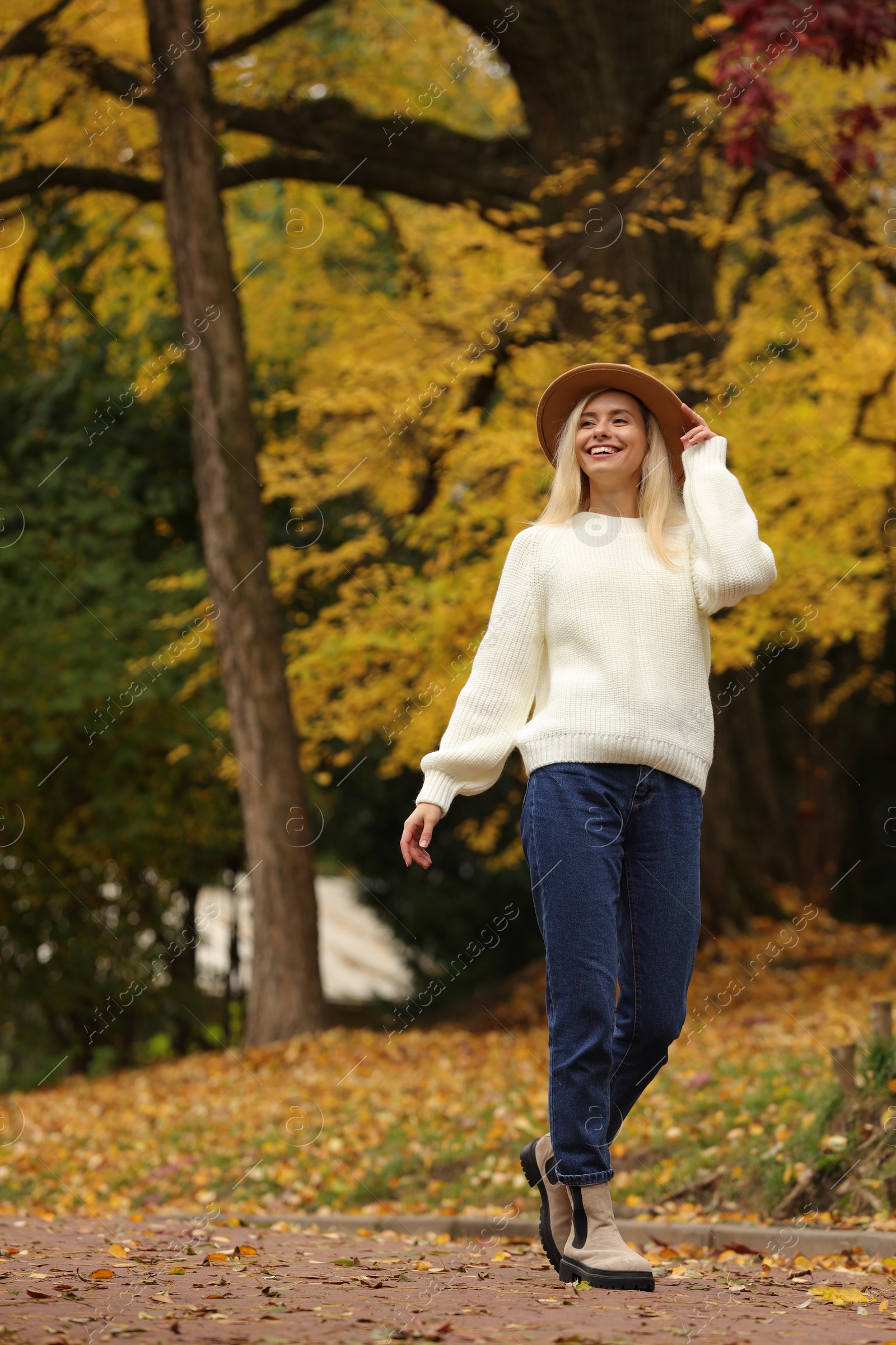 Photo of Happy woman wearing warm sweater walking in autumn park