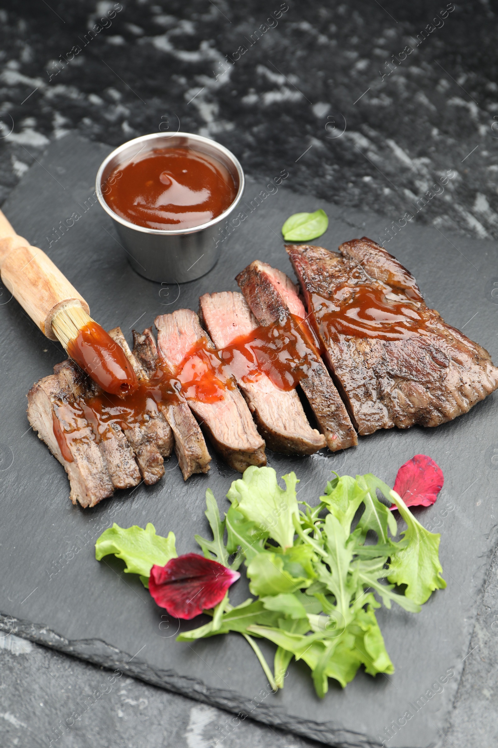 Photo of Pieces of delicious roasted beef meat with sauce and greens on black table