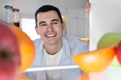 Happy man near refrigerator in kitchen, view from inside
