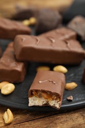 Photo of Slate board of chocolate bars with caramel, nuts and nougat on wooden table, closeup