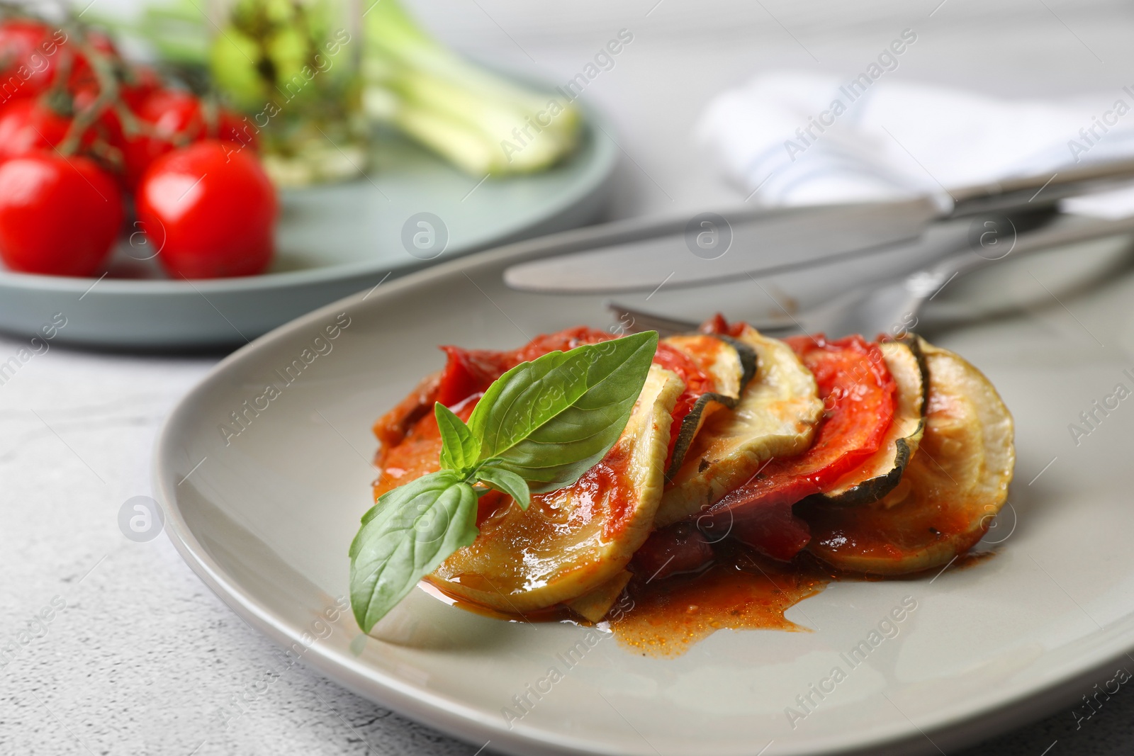 Photo of Delicious ratatouille served with basil on light grey table, closeup