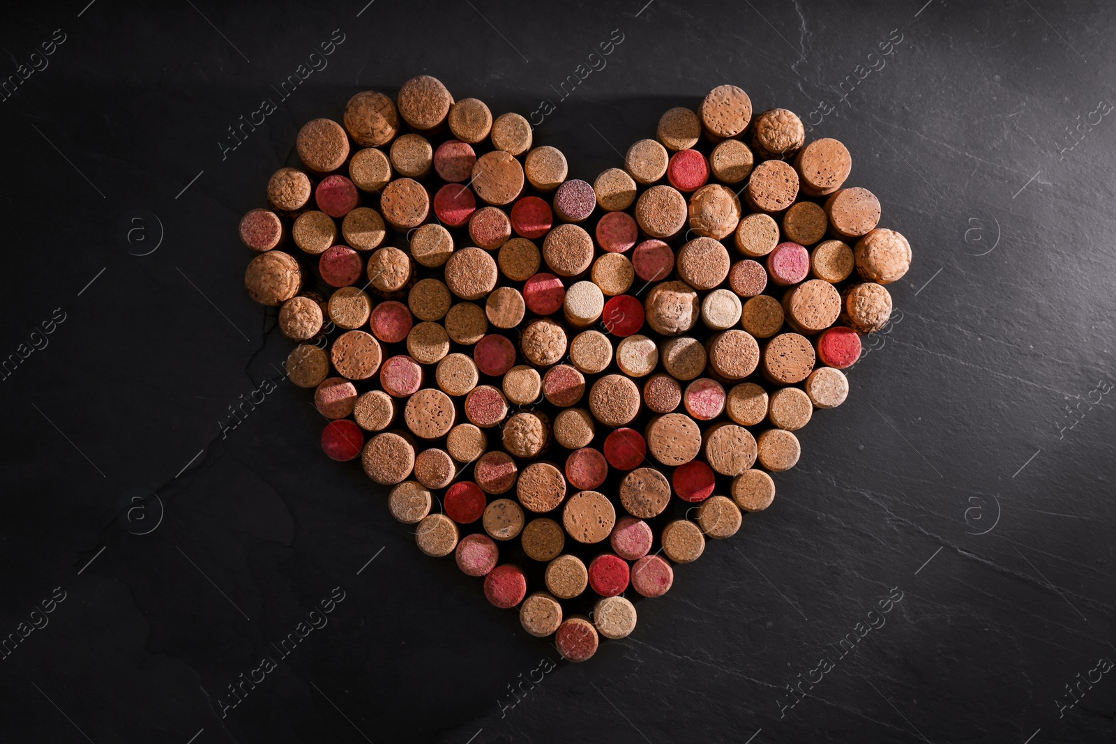 Photo of Heart made of wine bottle corks on black table, top view