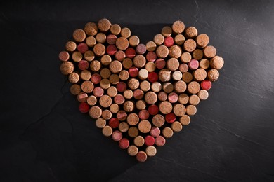 Heart made of wine bottle corks on black table, top view