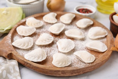 Photo of Raw dumplings (varenyky) with tasty filling and flour on wooden board, closeup