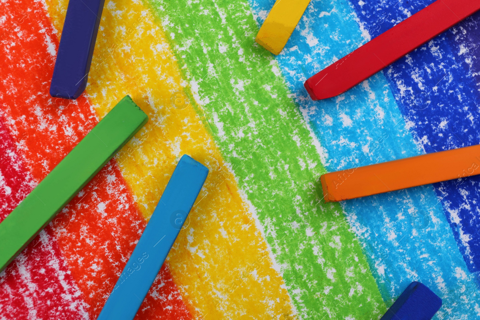 Photo of Colorful pastel chalks on drawing of rainbow, flat lay