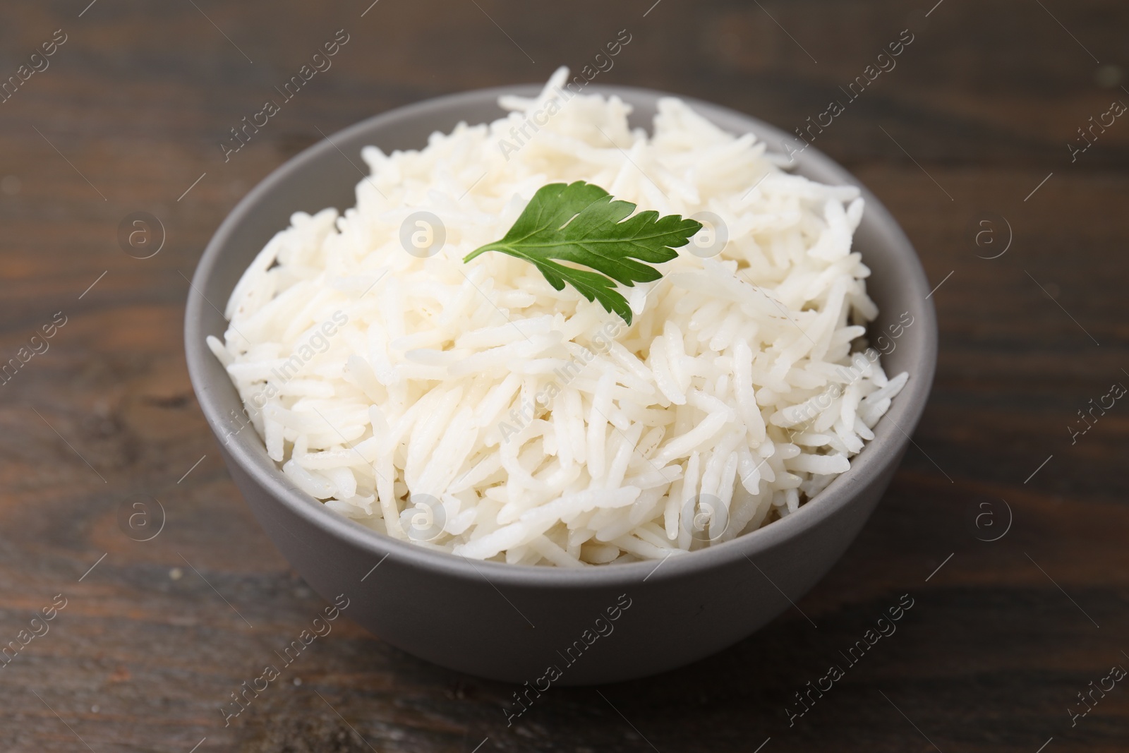 Photo of Bowl of delicious rice with parsley on wooden table, closeup