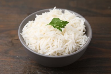 Photo of Bowl of delicious rice with parsley on wooden table, closeup