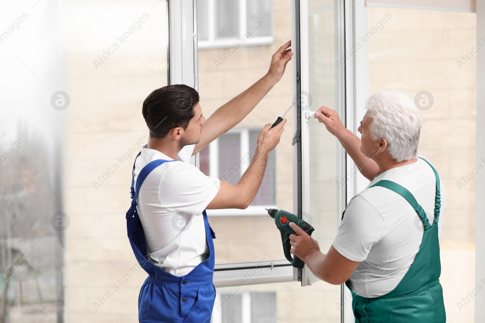 Photo of Construction workers repairing plastic window with screwdriver indoors