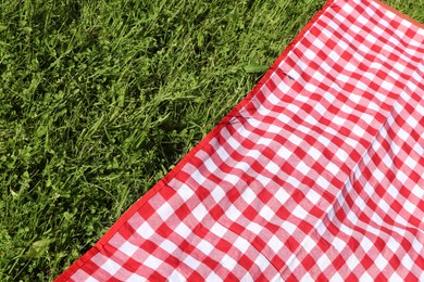 Photo of Checkered picnic tablecloth on fresh green grass, closeup. Space for text