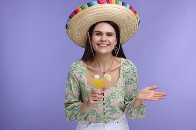 Photo of Young woman in Mexican sombrero hat with cocktail on violet background