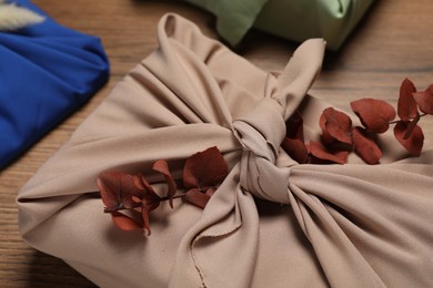 Photo of Furoshiki technique. Many gifts packed in fabric and dry leaves on wooden table, closeup