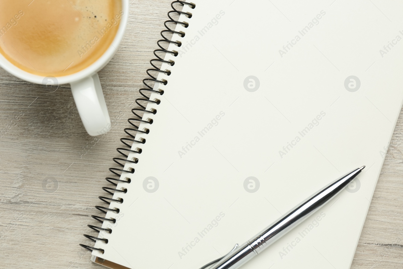 Photo of Blank notebook, cup of coffee and pen on white wooden table, flat lay