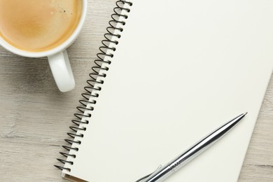 Blank notebook, cup of coffee and pen on white wooden table, flat lay