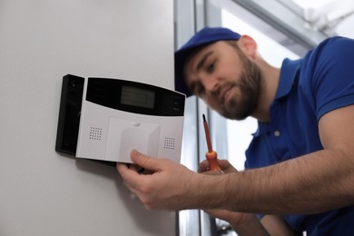 Photo of Man installing home security system on white wall in room