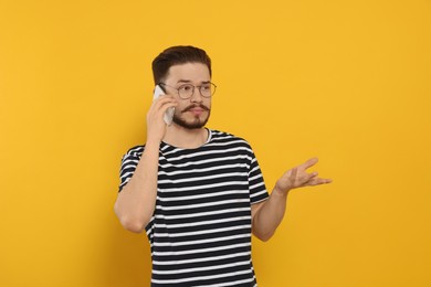 Photo of Dissatisfied man talking on phone against orange background. Space for text