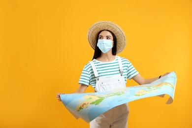 Female tourist in medical mask with map on yellow background, space for text. Travelling during coronavirus pandemic
