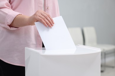 Photo of Woman putting her vote into ballot box on blurred background, closeup