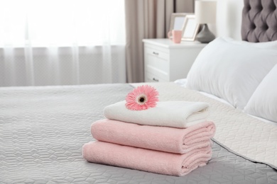 Photo of Stack of clean towels with flower on bed indoors. Space for text