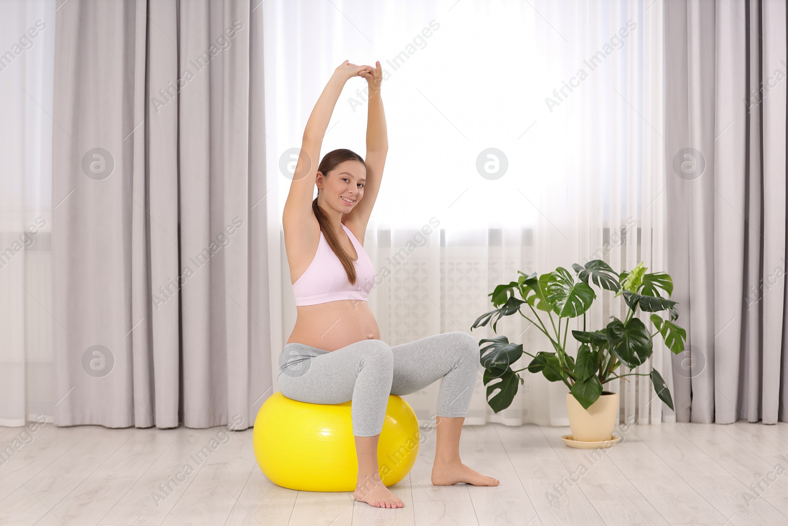 Photo of Pregnant woman doing exercises on fitness ball in room. Home yoga