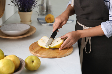 Photo of Woman cutting fresh ripe pear at table in kitchen, closeup