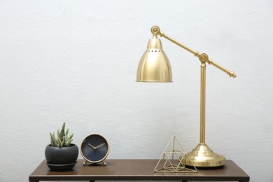 Photo of Beautiful plant in pot, lamp and accessories on wooden table near white wall indoors. Interior design