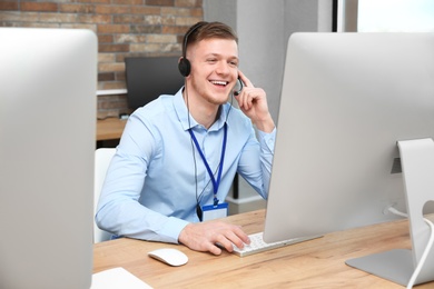 Photo of Technical support operator working with headset and computer at table in office