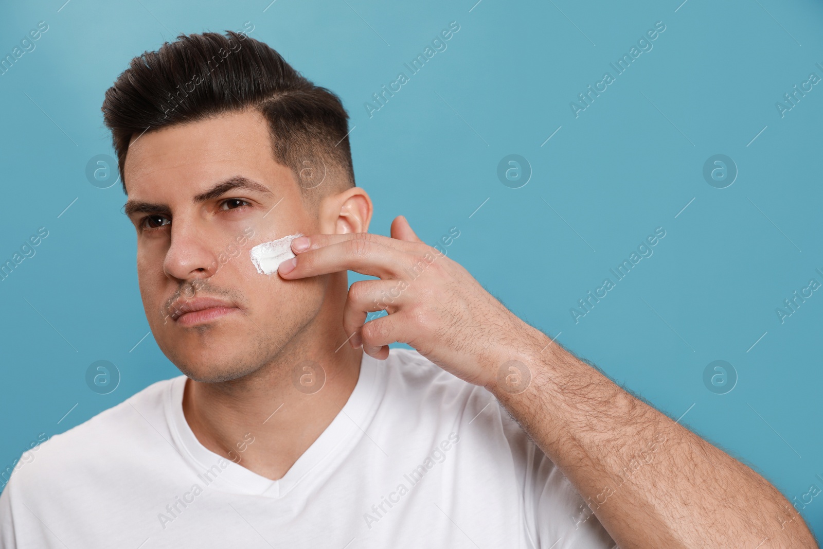 Photo of Handsome man applying face cream against turquoise background