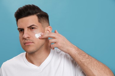 Handsome man applying face cream against turquoise background