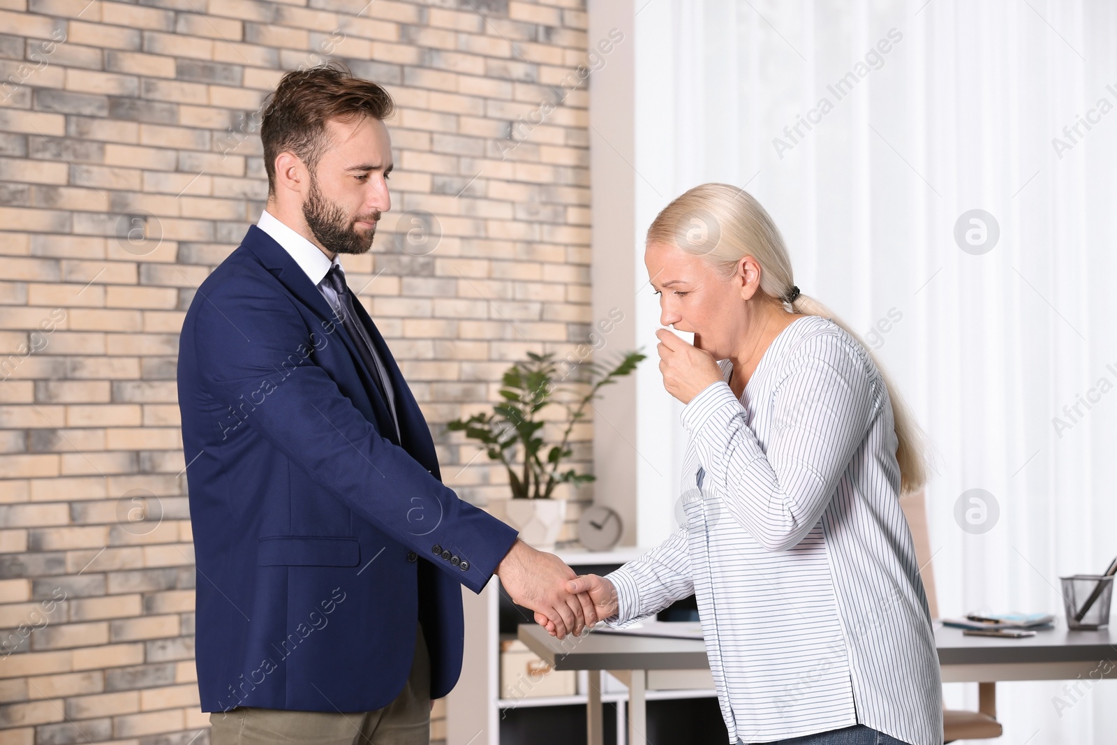 Photo of Young man handshaking with ill mature woman suffering from cough in office
