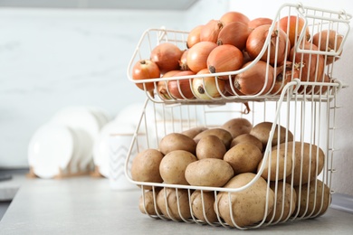 Photo of Container with potatoes and onions on grey kitchen counter, space for text. Orderly storage