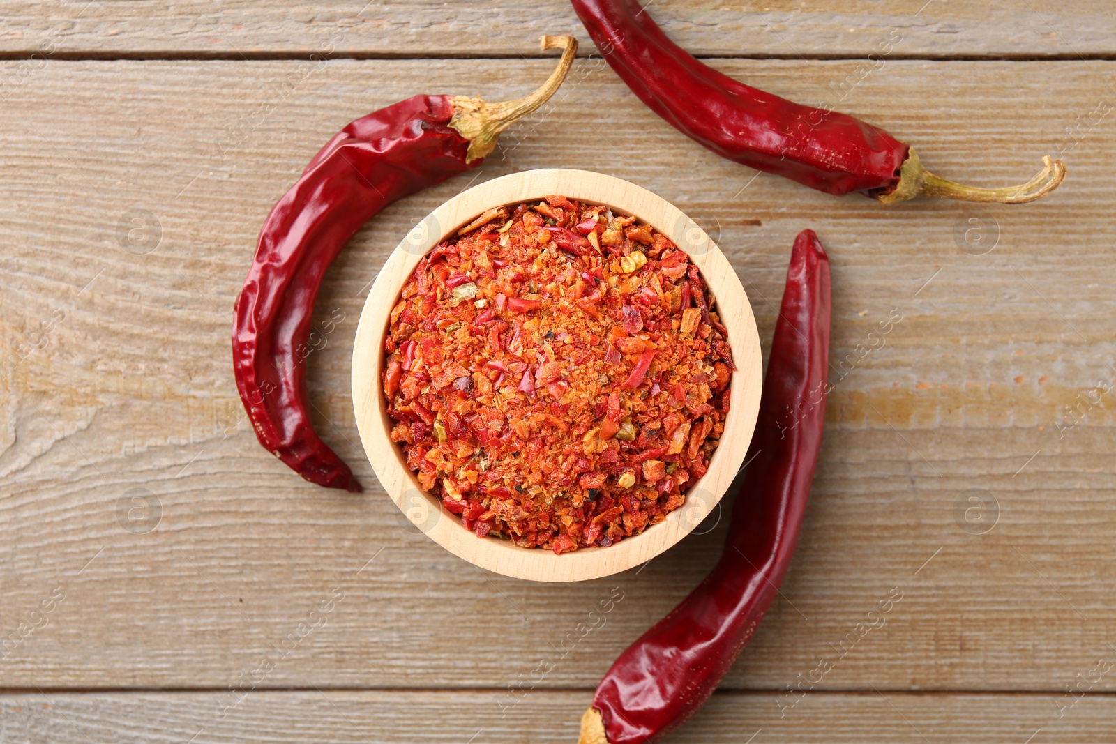 Photo of Aromatic spice. Red chili pepper flakes in bowl and pods on wooden table, top view