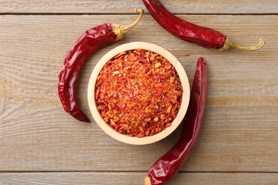 Aromatic spice. Red chili pepper flakes in bowl and pods on wooden table, top view