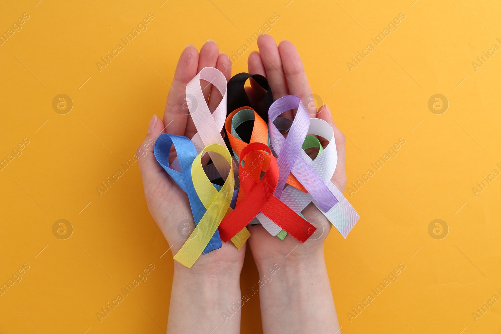 Photo of Woman with many colorful awareness ribbons on orange background, top view