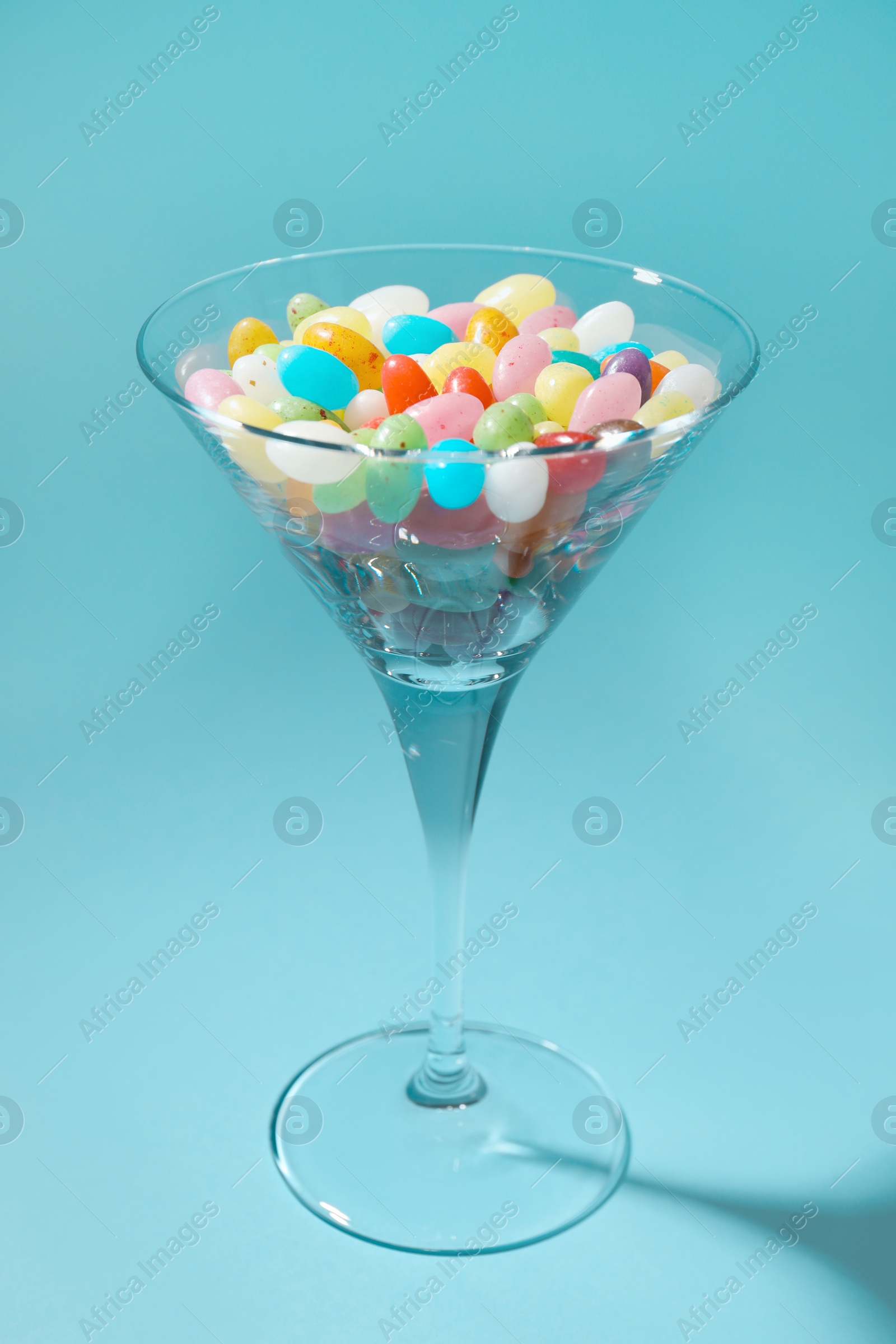 Photo of Beautiful martini glass with colorful candies on light blue background