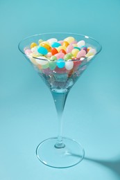 Beautiful martini glass with colorful candies on light blue background