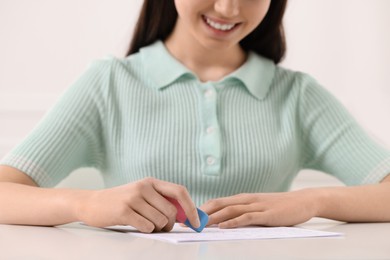 Photo of Teenage girl erasing mistake in her notebook at white desk, closeup