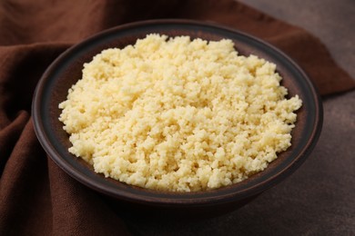 Tasty couscous in bowl on brown table, closeup