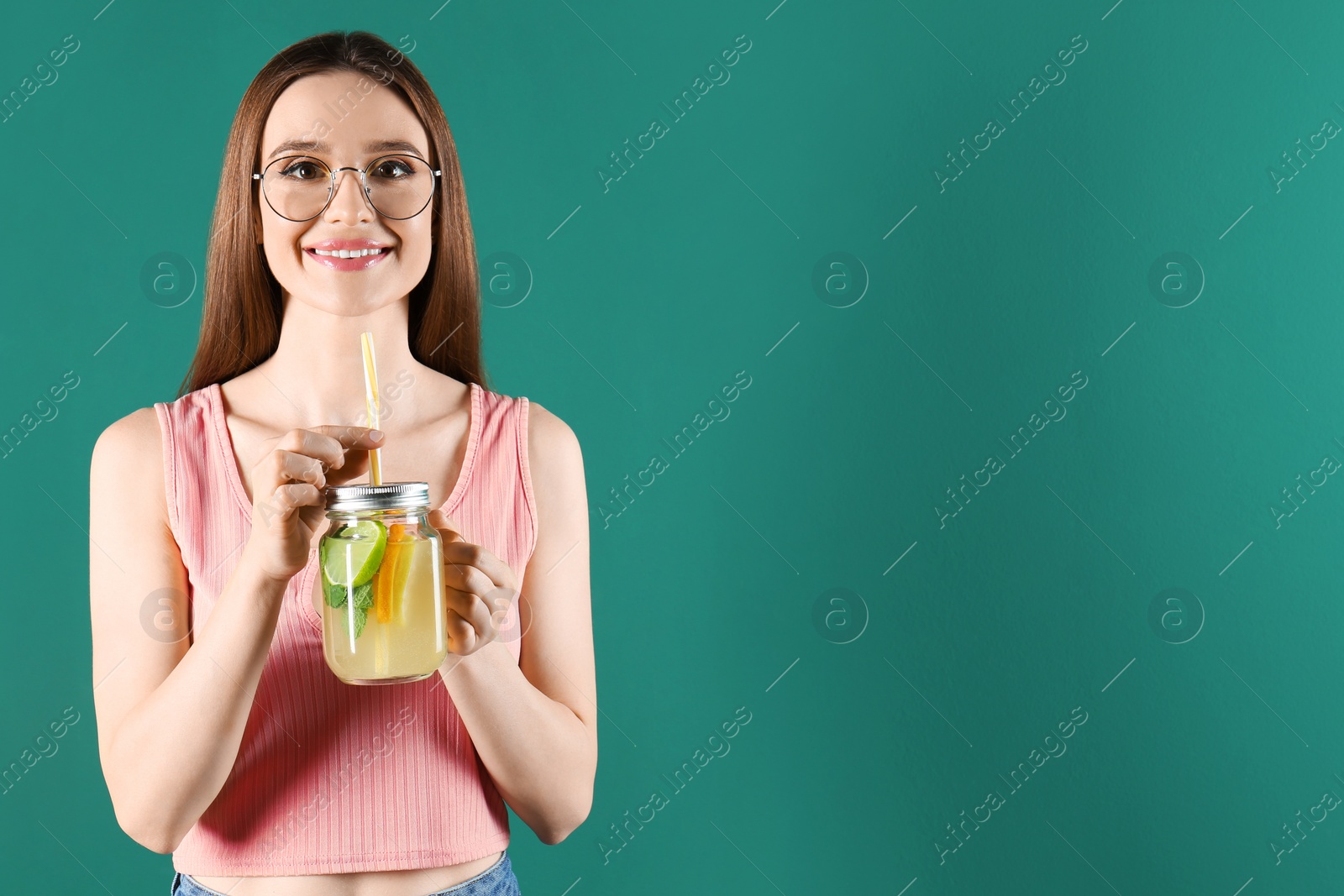 Photo of Beautiful young woman with Mason jar of natural detox lemonade on green background. Space for text