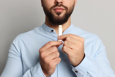 Photo of Young man applying lip balm on grey background, closeup