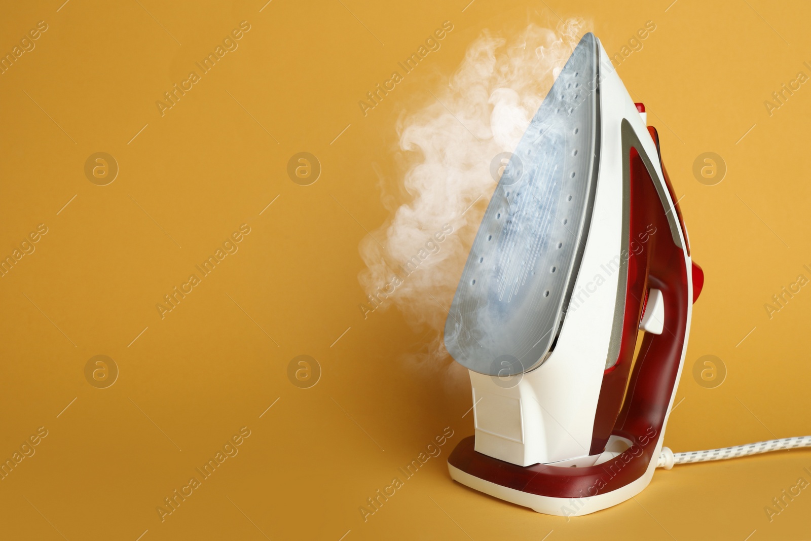 Image of Modern iron with steam on orange background, space for text