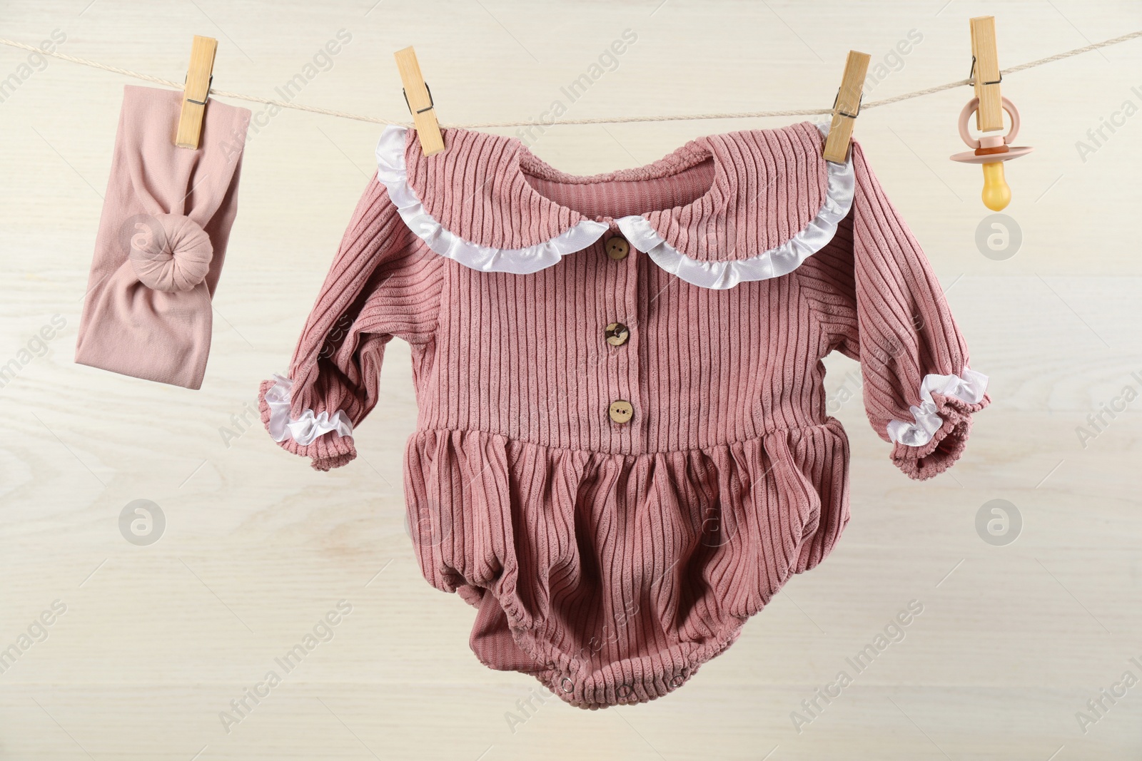 Photo of Baby clothes and accessories hanging on washing line near white wooden wall