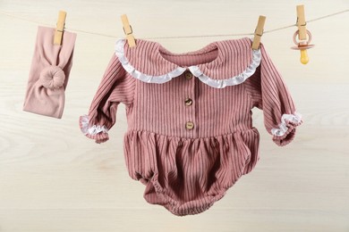 Photo of Baby clothes and accessories hanging on washing line near white wooden wall