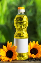 Photo of Bottle of cooking oil, sunflowers and seeds on wooden table against blurred background