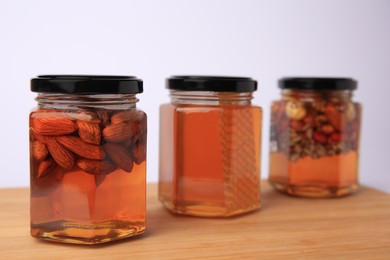 Jars with different nuts and honey on wooden table against white background