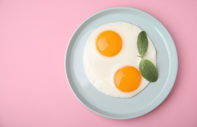 Photo of Tasty fried eggs with basil in plate on pink background, top view. Space for text