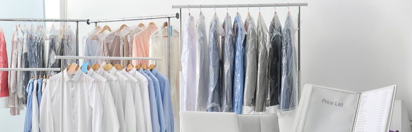 Image of Racks with clean clothes on hangers indoors, banner design. Dry-cleaning service