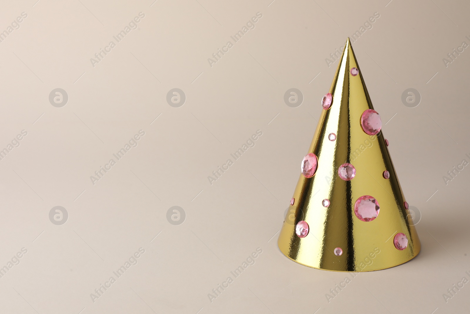 Photo of One shiny golden party hat with rhinestones on beige background. Space for text