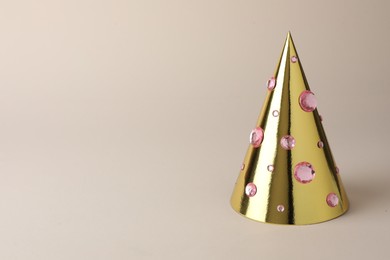 Photo of One shiny golden party hat with rhinestones on beige background. Space for text