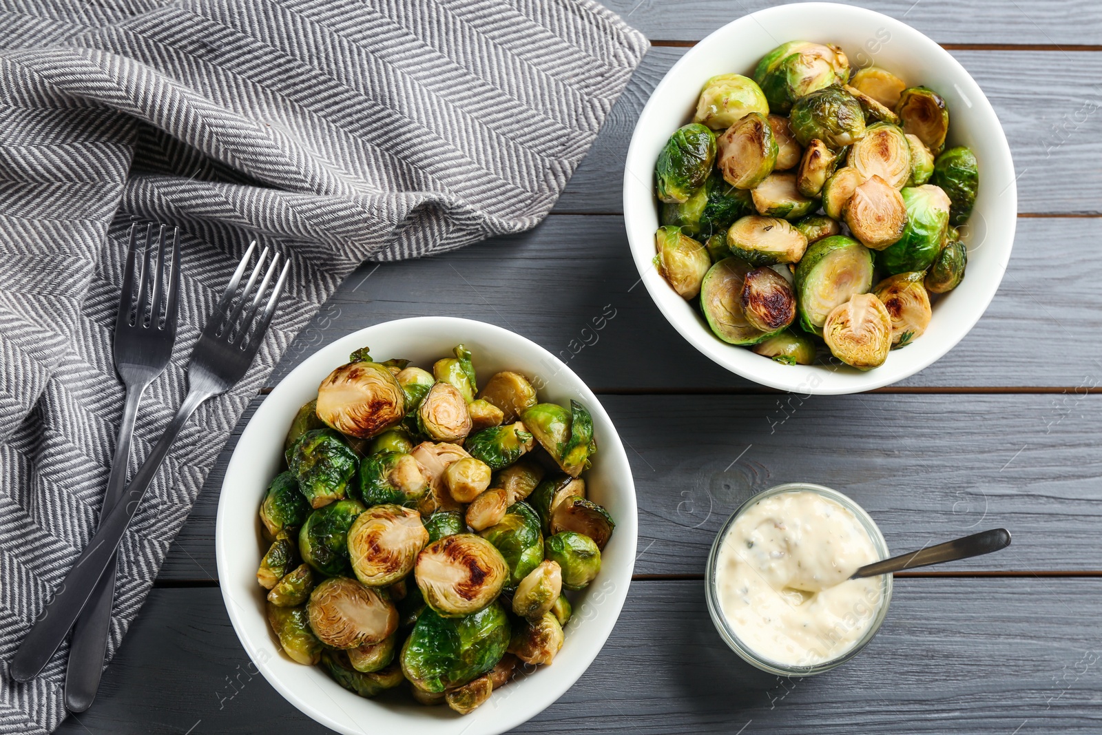 Photo of Delicious roasted Brussels sprouts served on grey wooden table, flat lay